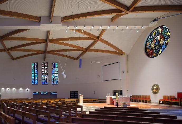 Unutrašnjost suvremene crkve s drvenim stropnim gredama, drvenim klupama i oslikanim prozorima