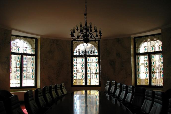 Unutrašnjost prostorije s konferencijskim stolom i naslonjačima, tri prozora s vitrajima i kristalnim lusterom