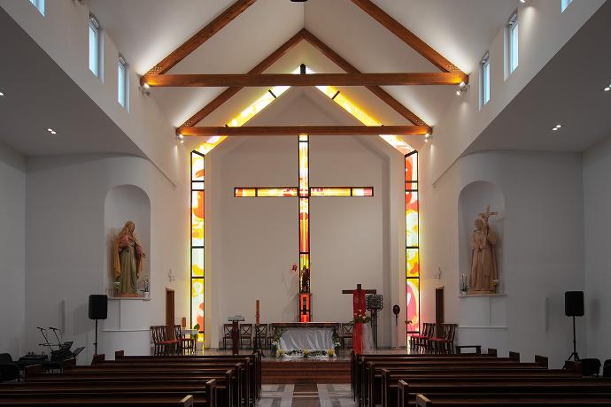 Unutrašnjost suvremene crkve s drvenim gredama, statuama svetaca i vitrajem iza oltara