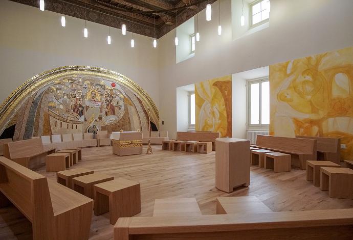 Svetište sa prozorima, drvenim podom, modernim drvenim klupama, oslikanim zidovima i svjetiljkama koje vise s drvenog stropa