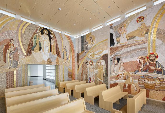 Unutrašnjost prostorije s drvenim klupama i zidova prekrivenim mozaicima s biblijskim scenama