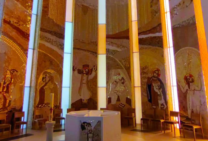 Unutrašnjost moderne crkve s uskim prozorima i zidovima obloženim mozaicima