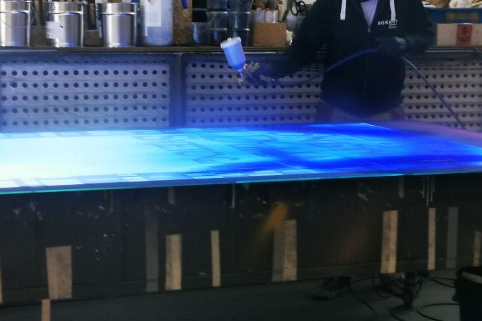 Čovjek pomoću ručnog uređaja nanosi plavu boju na osvijetljenu površinu
